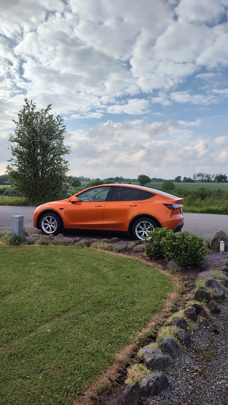Susanne ved sin orange Tesla med et fyrtårn i baggrunden